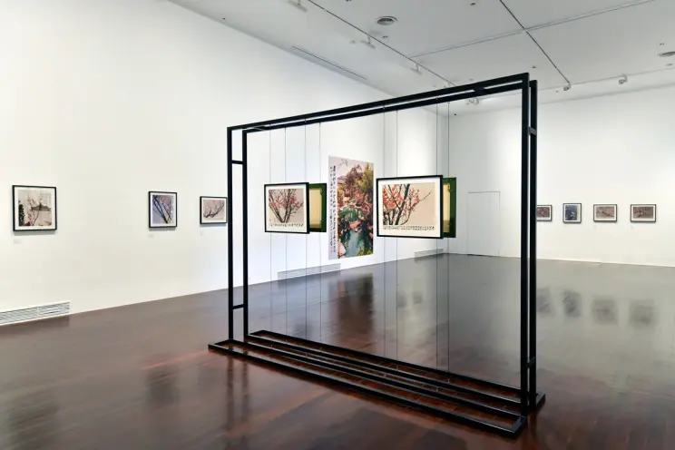 A spacious white gallery room with polished wooden flooring showcases an exhibition of framed photographs depicting Japane...