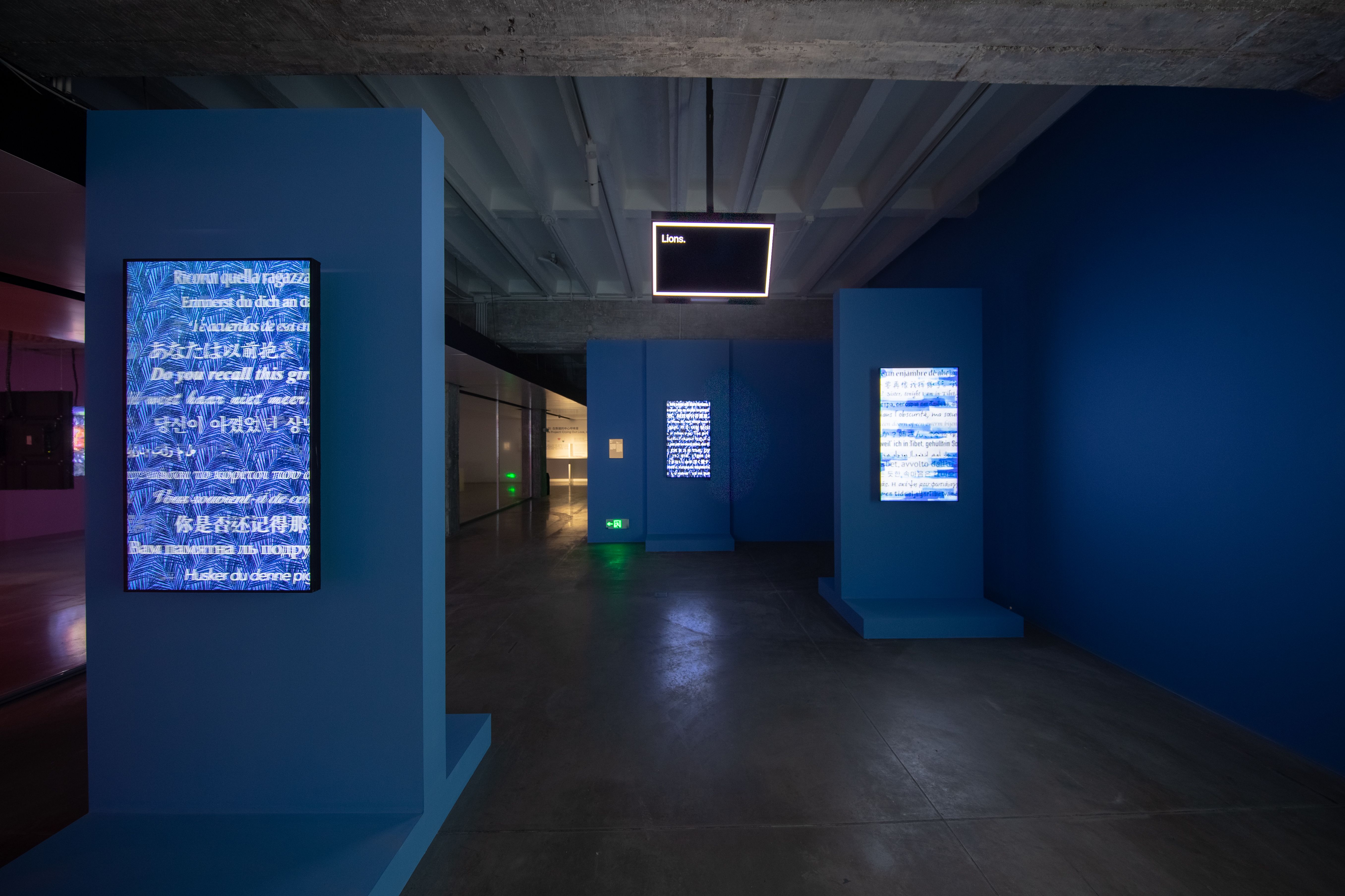 Art exhibit hallway with blue pillars displaying text and overhead neon sign.