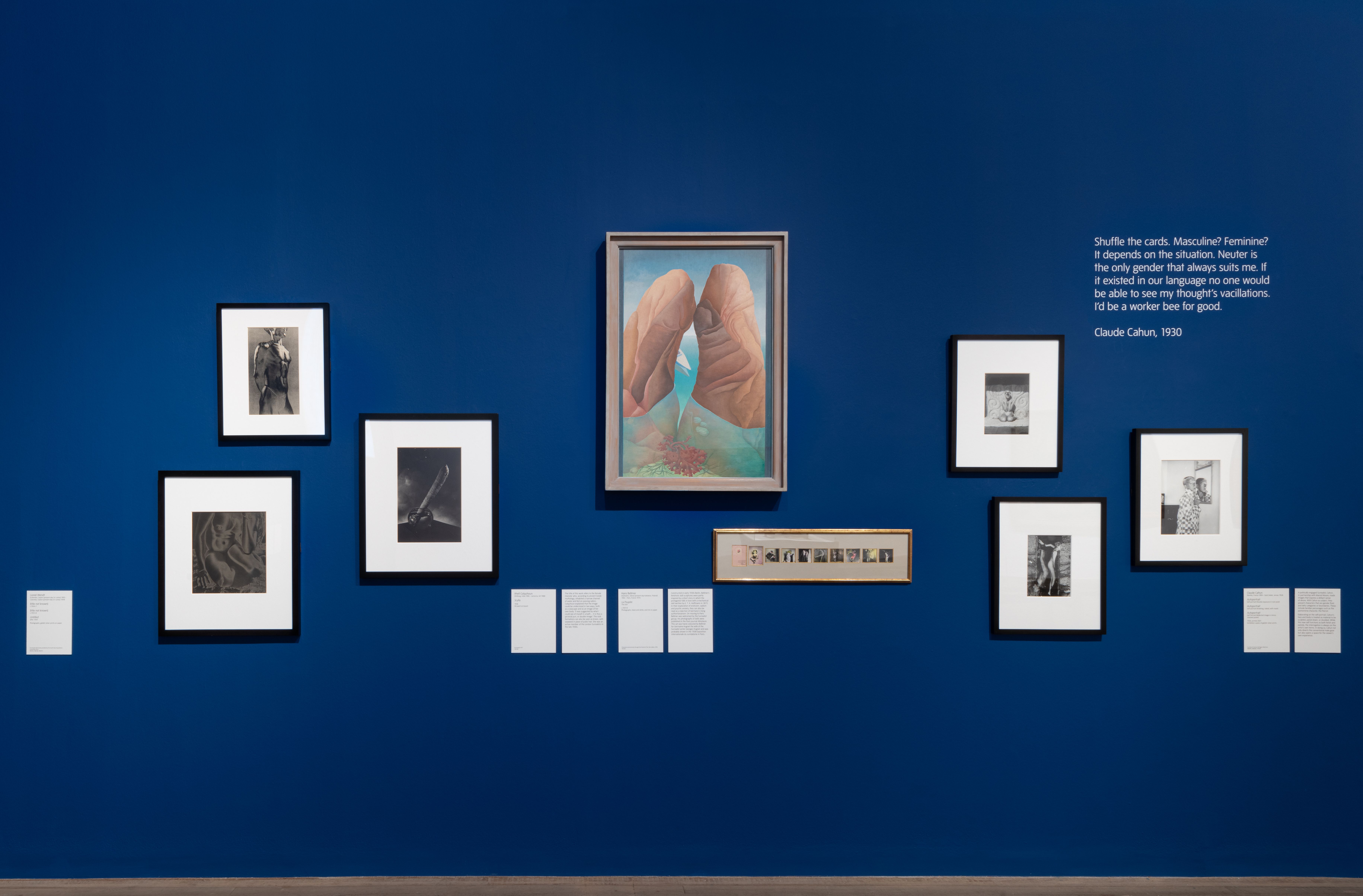 An assortment of framed art pieces of various shapes and sizes hang in a distinct pattern on a vibrant blue wall.