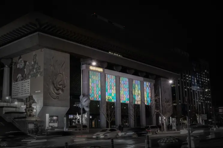 A building facade with architectural pillars, illuminated with pastel-colored images.