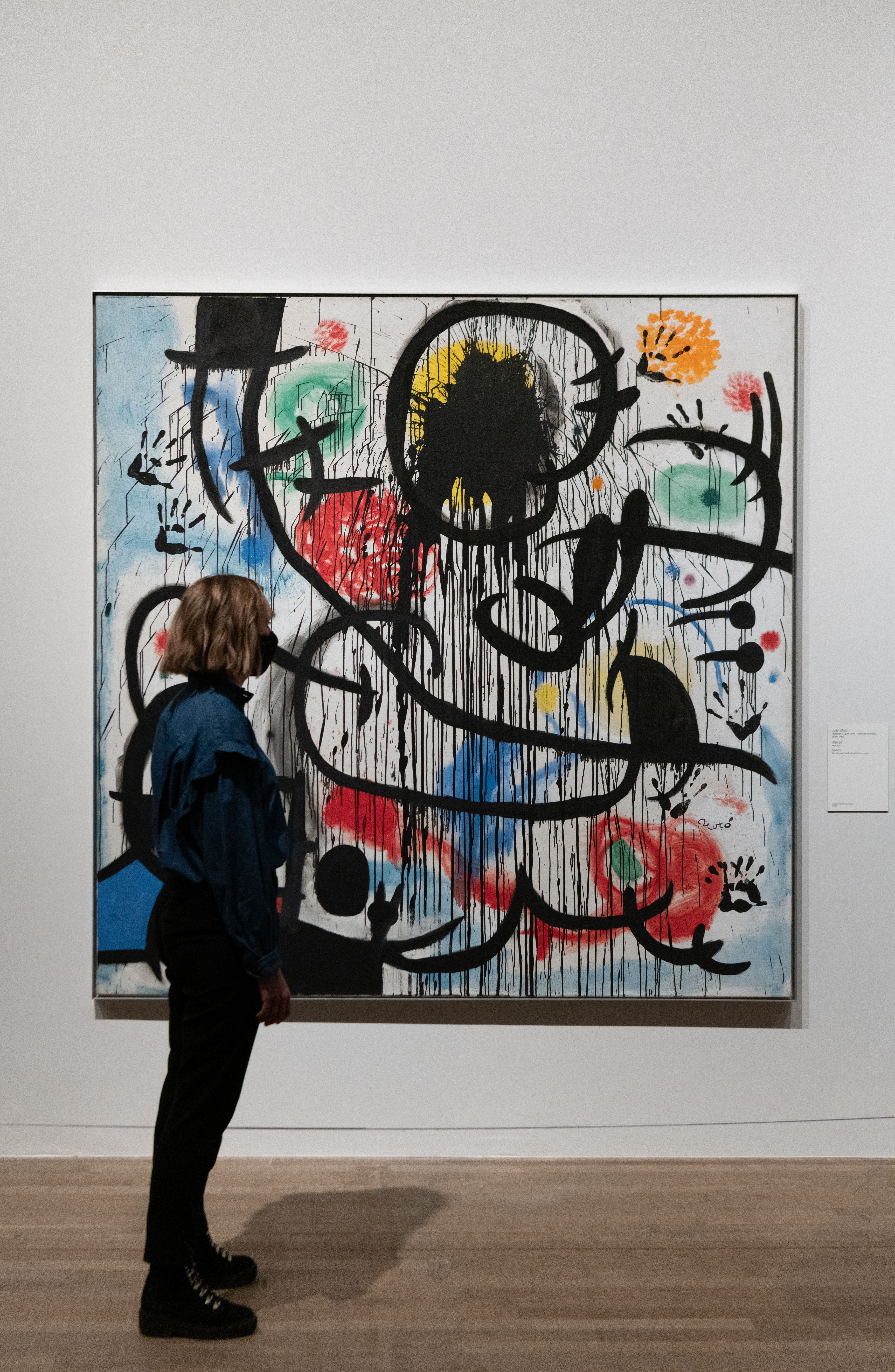 A person seen in profile is standing in front of a large, abstract artpiece hanging on the wall.