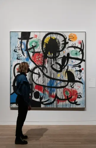 A person seen in profile is standing in front of a large, abstract artpiece hanging on the wall.