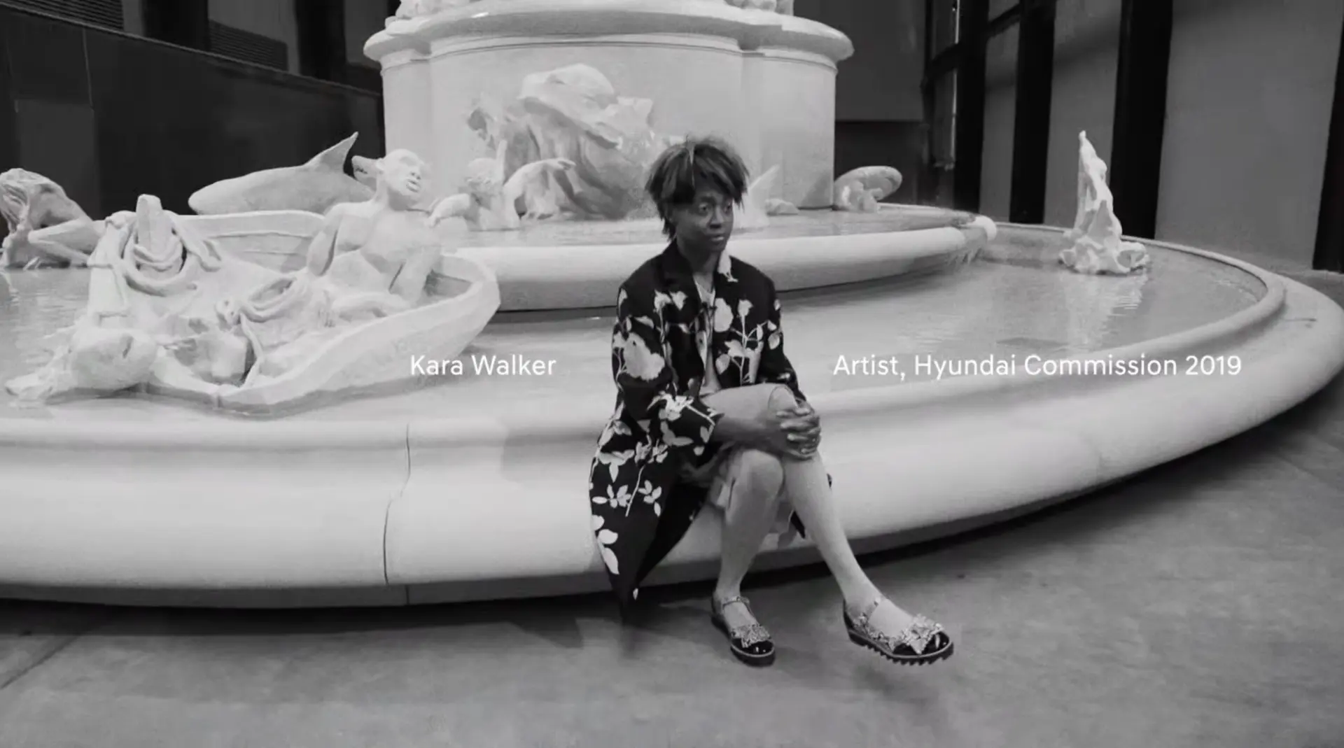 An individual is seated on a large sculpture. A caption overlay reading "Kara Walker Artist, Hyundai Commission 2019" is v...