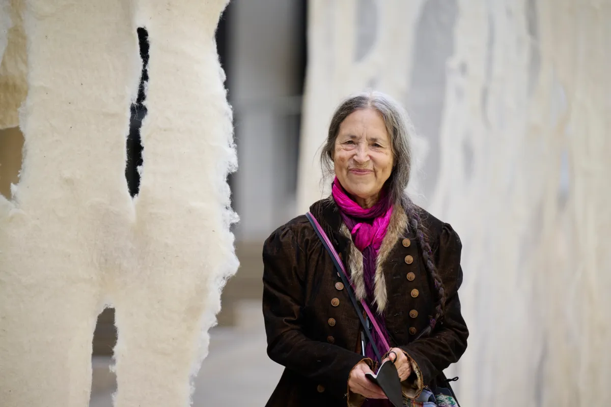 A woman is standing next to a felt curtain in an art installation.