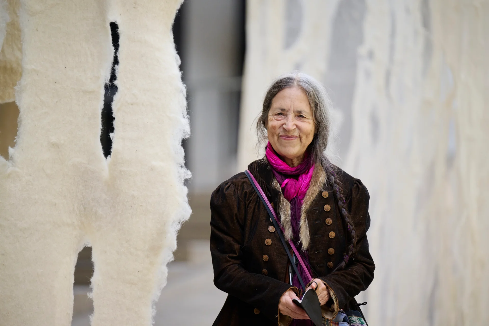 A woman is standing next to a felt curtain in an art installation.