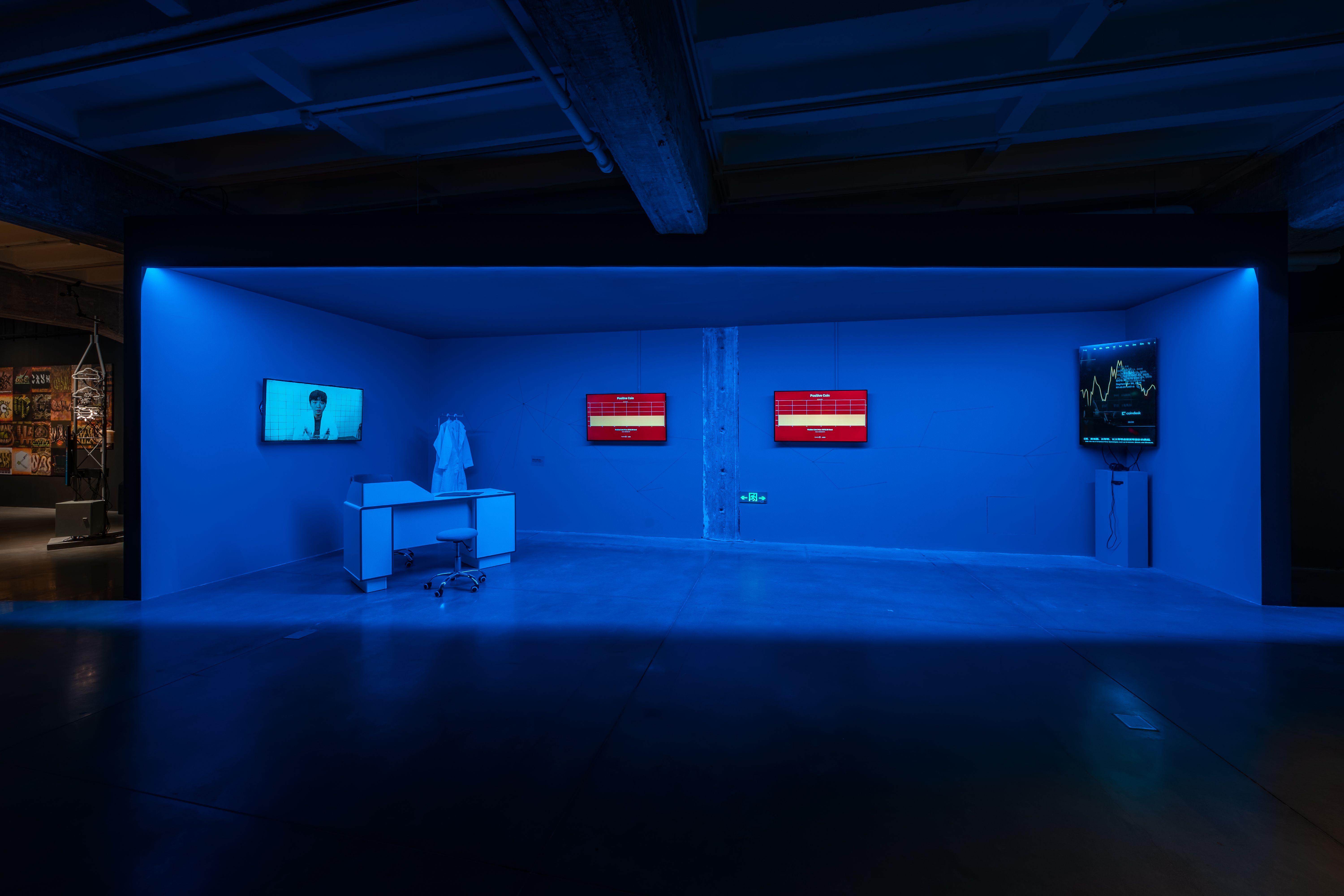 Art exhibit with blue lighting and screens showing financial and scientific data.