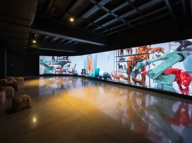 Gallery room with large wall mural of animals and hay bales on floor.