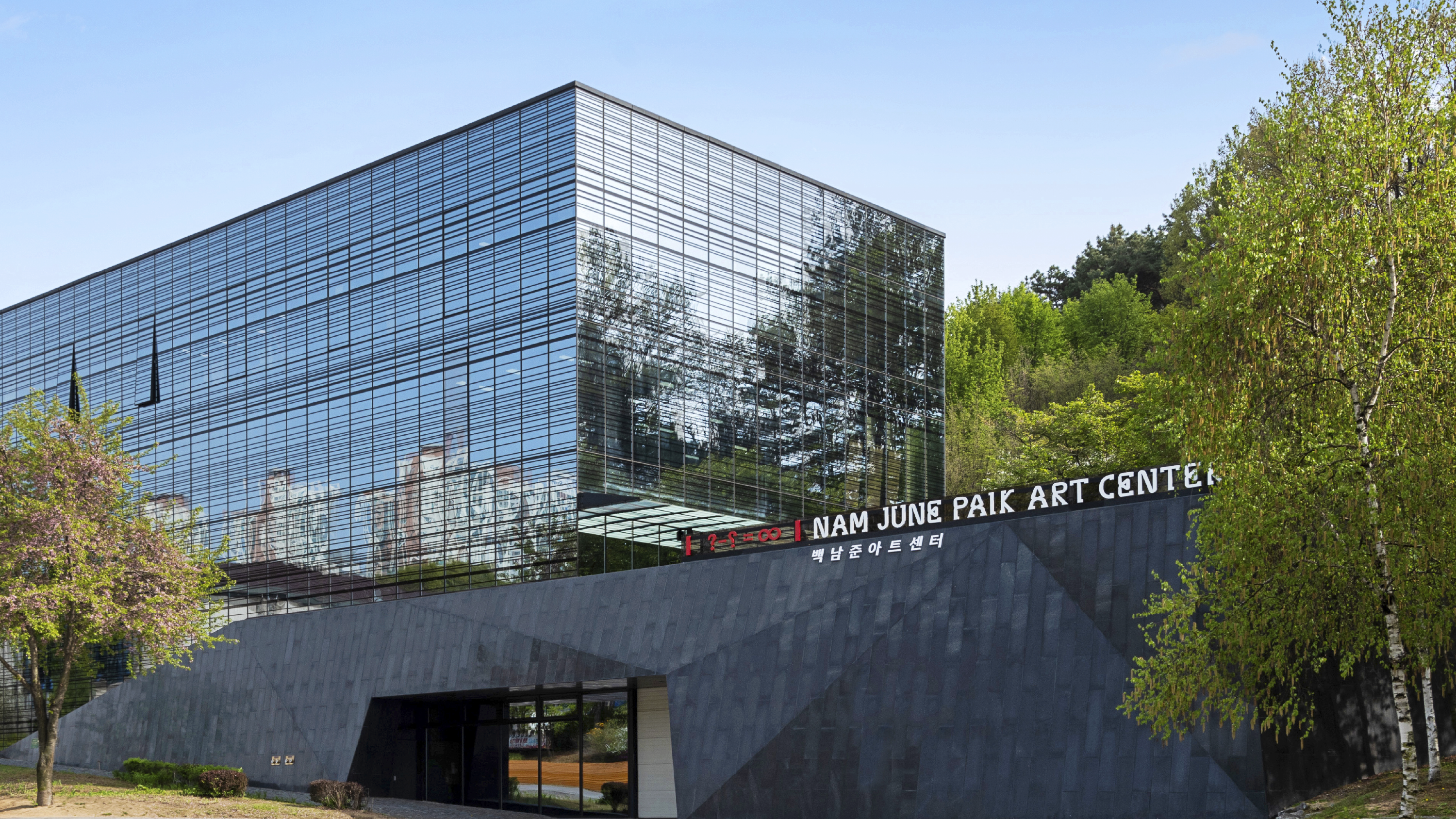 Exterior view of the Nam June Paik Art Center, a modern building with a sleek, angular design. The lower section is clad i...