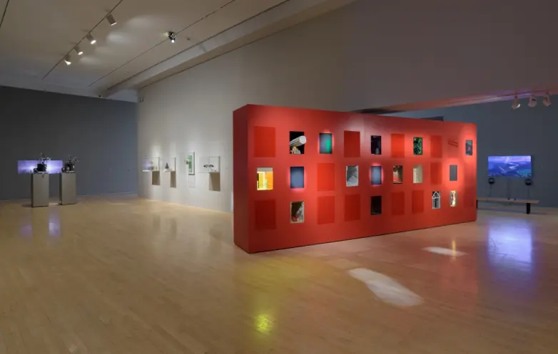 A gallery room showcasing various art pieces, with a prominent red exhibition wall.