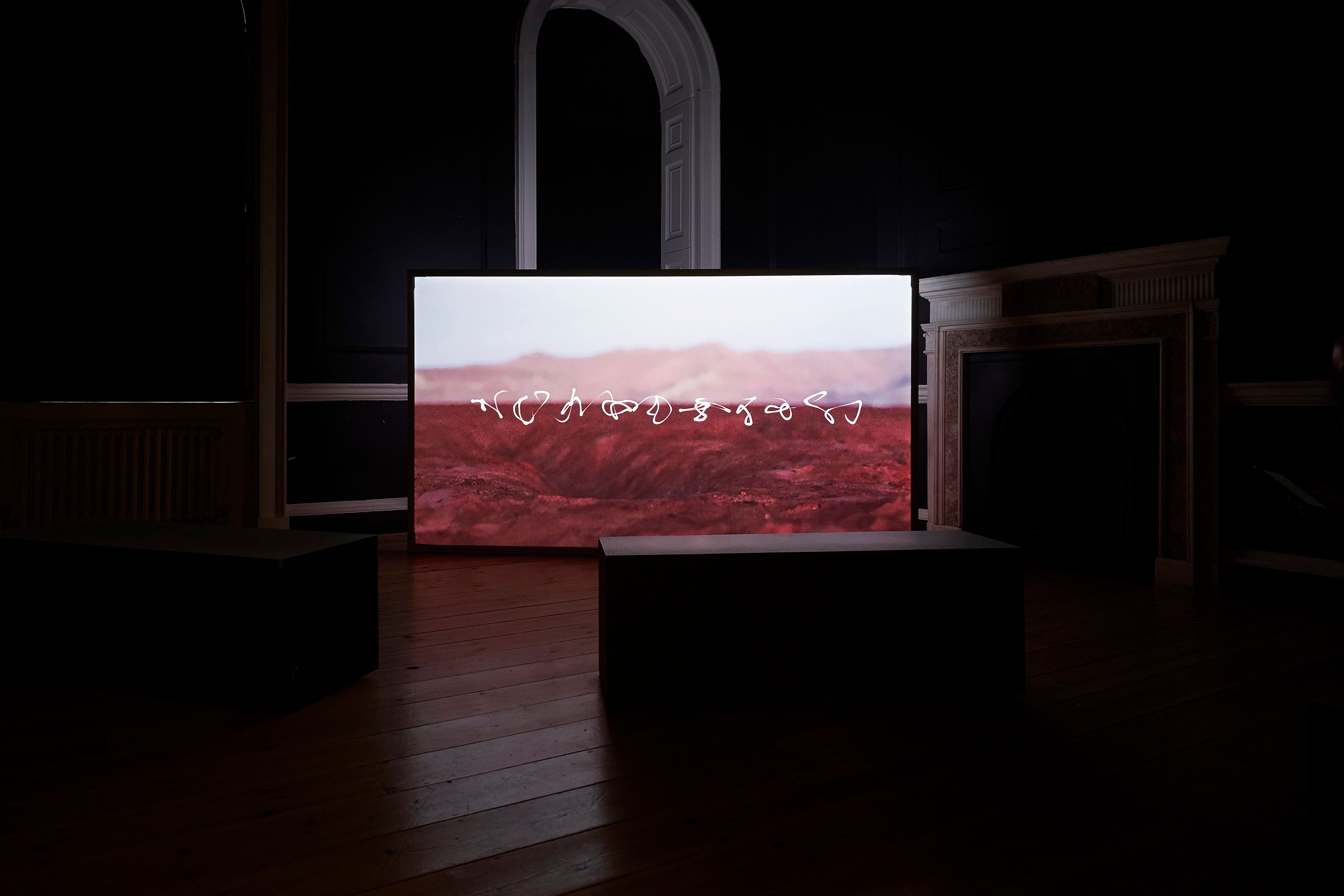 A large screen in a dark room displaying white abstract lines over a red desert terrain.