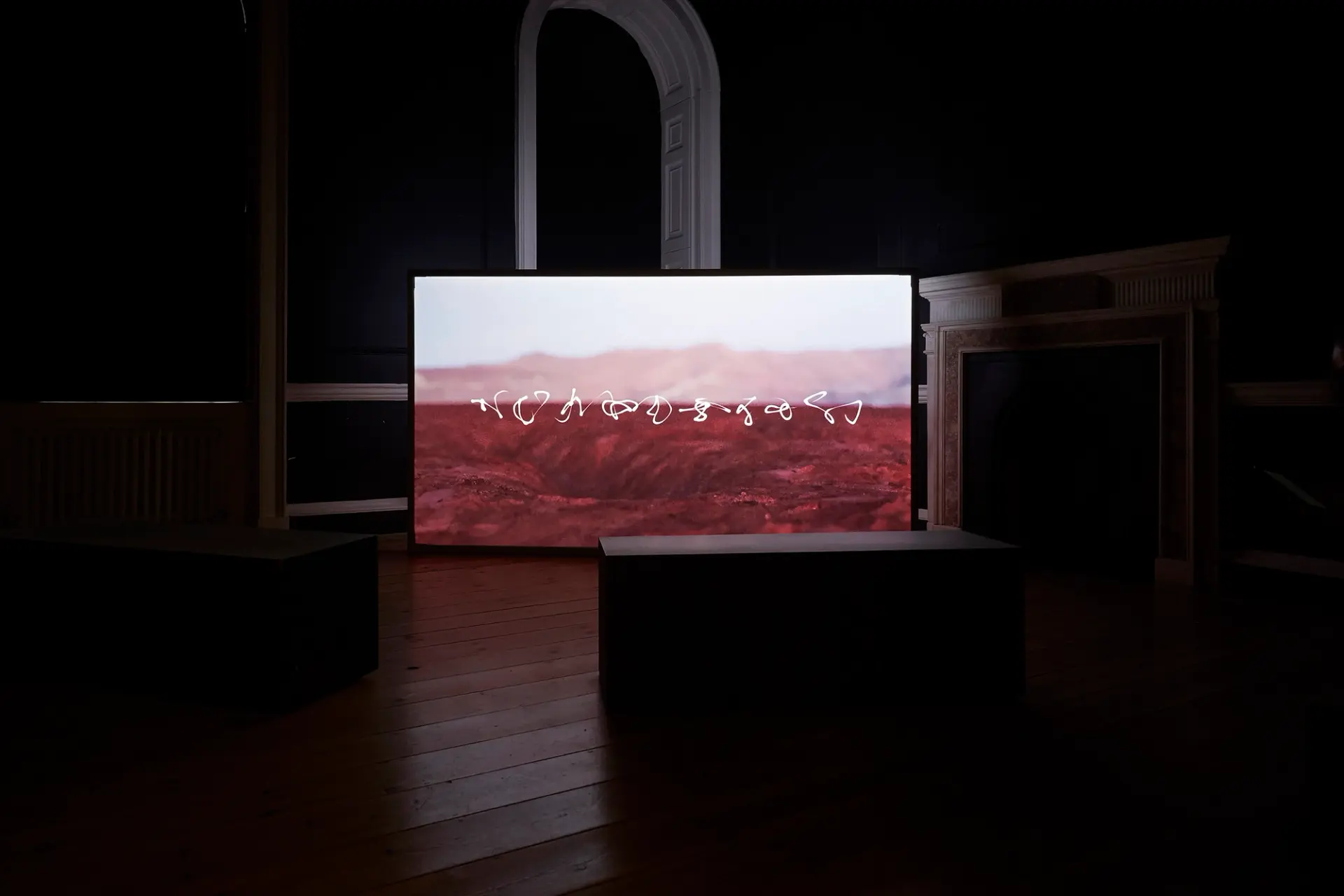 A large screen in a dark room displaying white abstract lines over a red desert terrain.