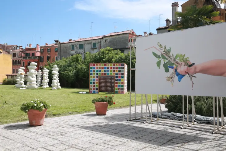Outdoor art exhibit with stone sculptures, colorful panels, and a painting of a hand with plants in a garden.