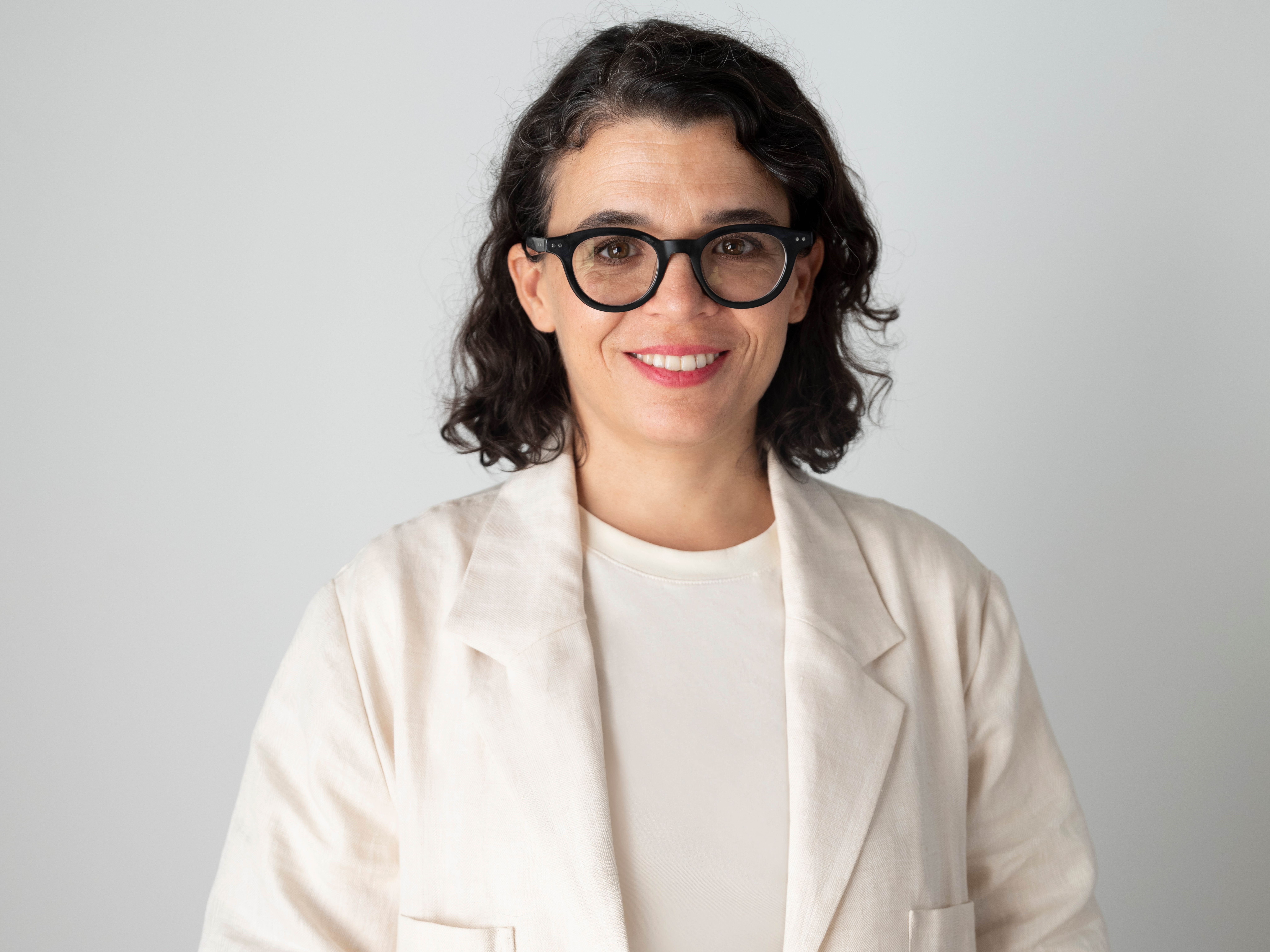 A person smiling at the camera in a white top and black round glasses.