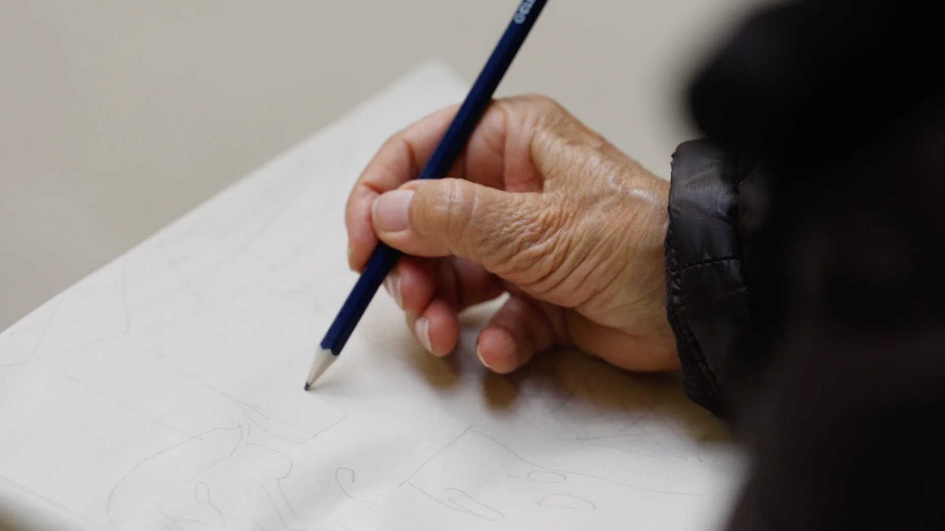 A hand sketching with a pencil on a white paper.
