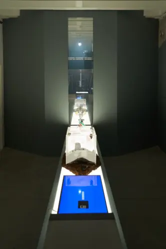 Long translucent boxes with various contents on display in gallery.