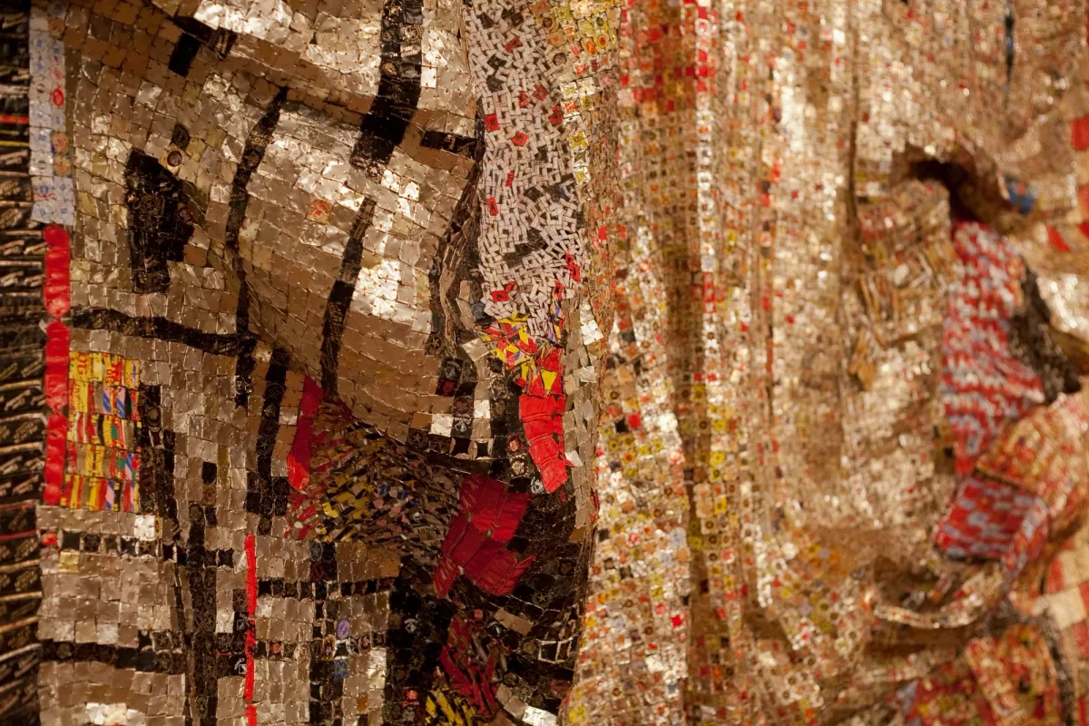 Detail of El Anatsui's artwork composed of aluminium and copper wire, exhibiting patterns in golden, brown, red, and yellow hues.