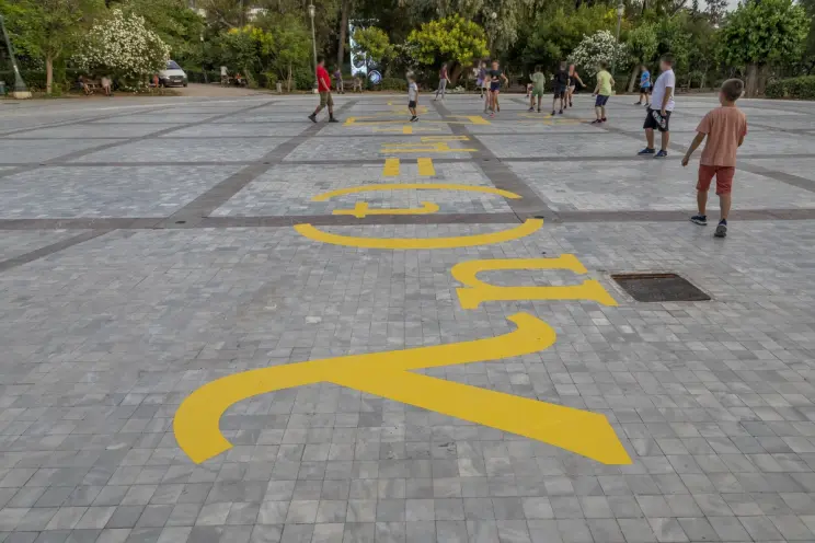 Children playing on a tiled plaza with large yellow mathematical symbols painted on the ground.