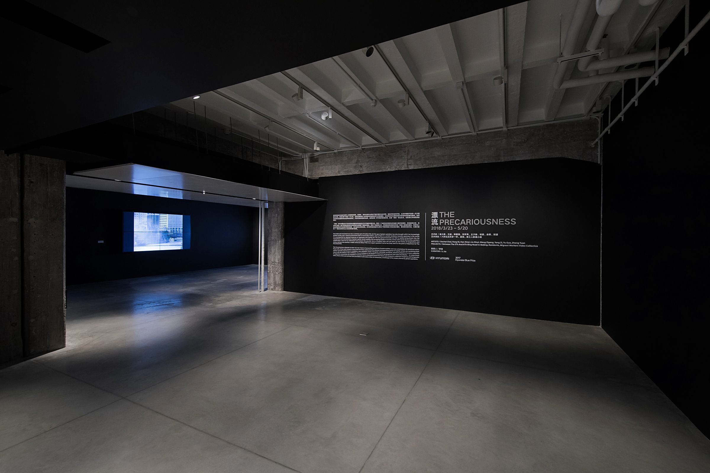 Dark gallery room with a lit text wall and video projection.