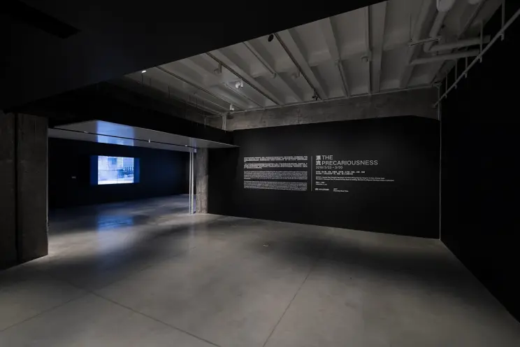 Dark gallery room with a lit text wall and video projection.