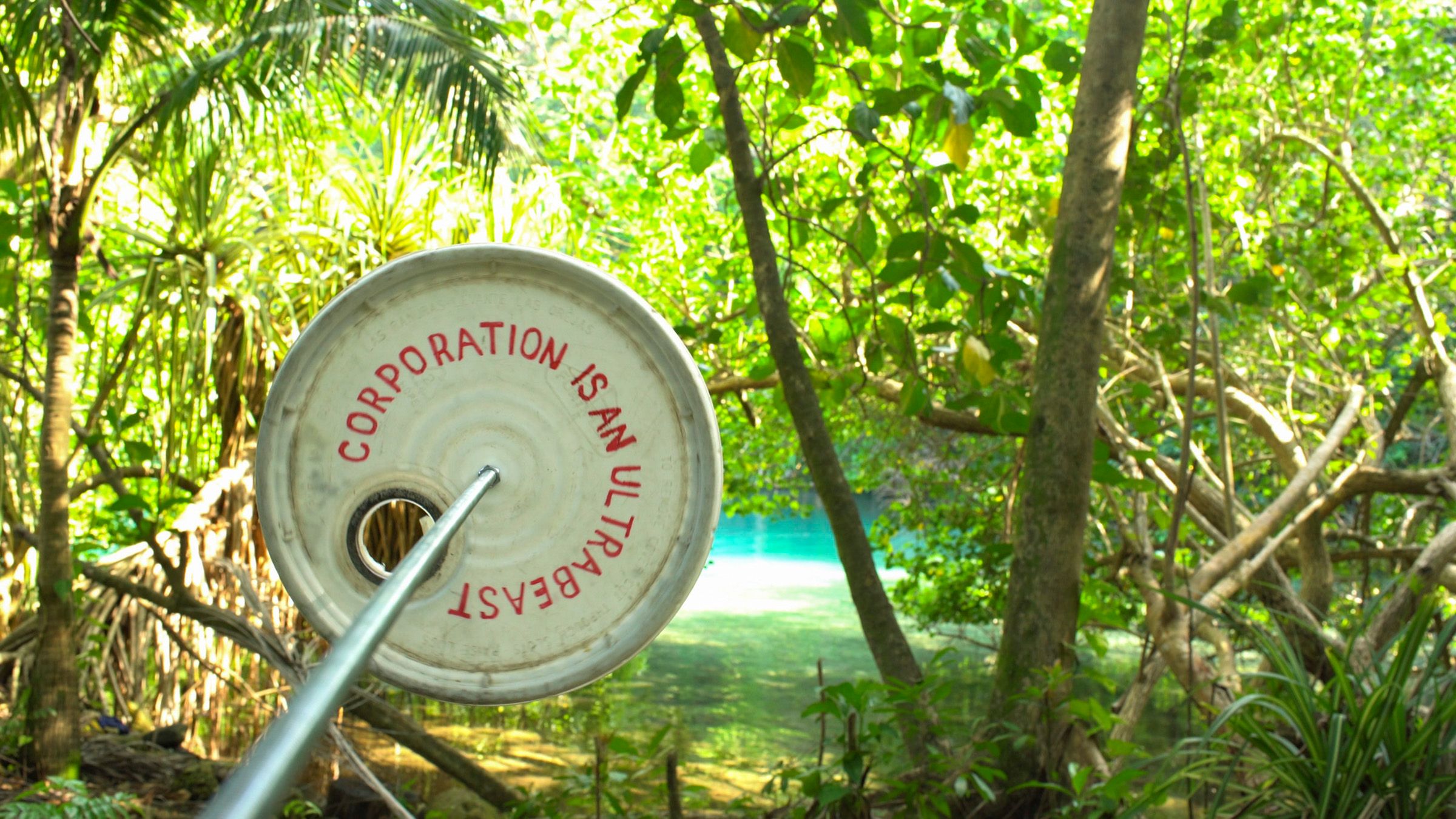 A white metal disk with the red caption "CORPORATION IS AN ULTRABEST" set against a tropical background.