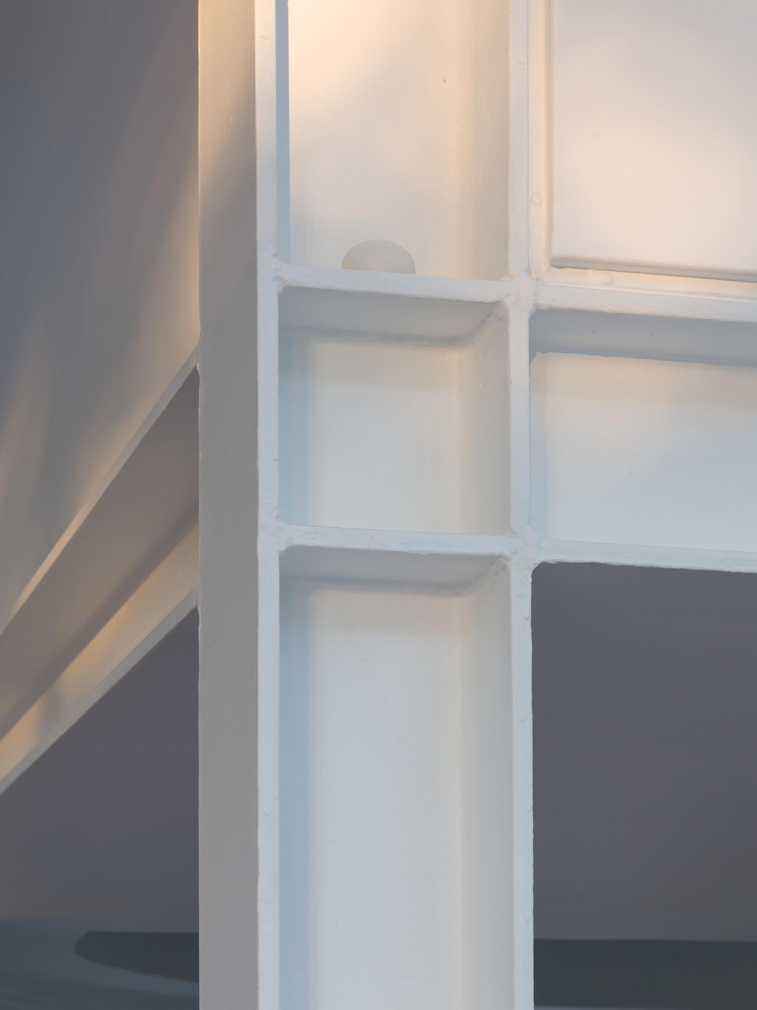 Close-up of a white sphere resting on a ledge where two white walls intersect, with soft light creating shadows.