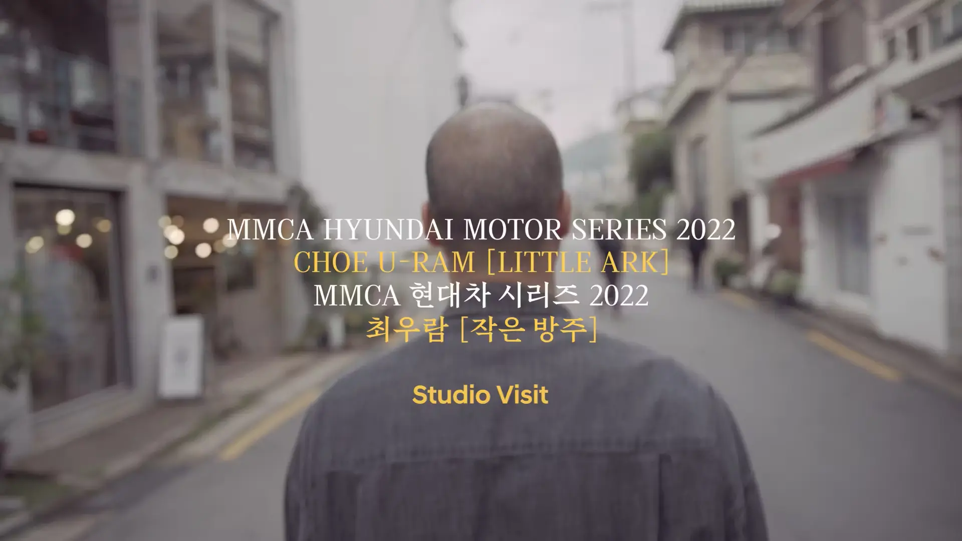 A street scene viewed from behind a person. A caption across the image reads "MMCA Hyundai Motor Series 2022: Choe U-Ram -...