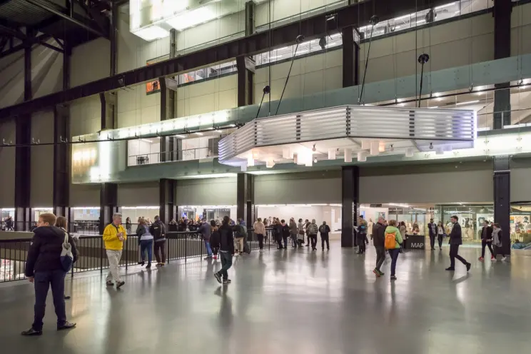 A bustling gallery hall filled with a crowd of visitors, admiring the artwork and interacting with each other.