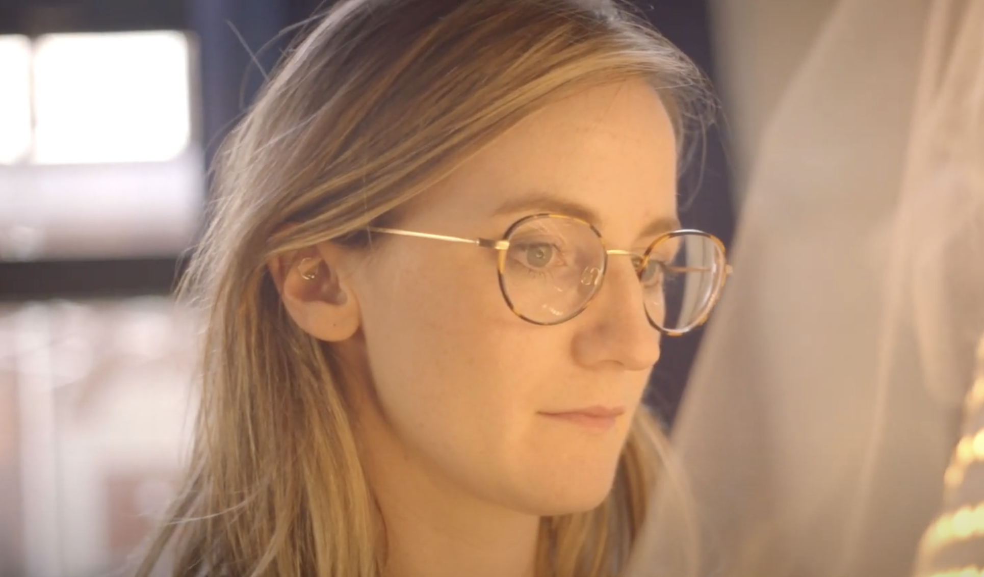 A portrait of an individual with long hair, gazing to the side while sporting glasses.