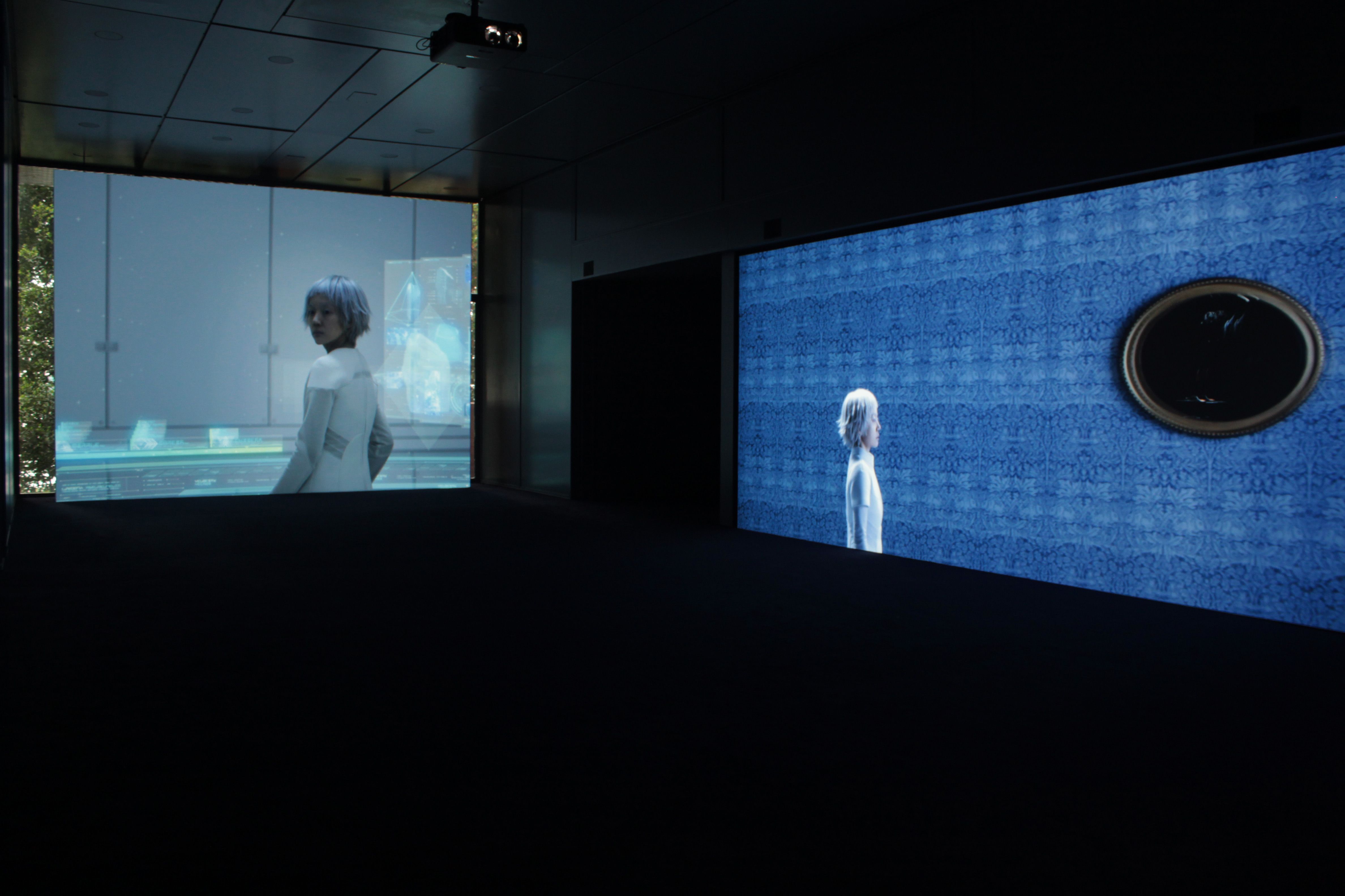 Two projections of an individual with white hair, one displayed on a frontal white canvas and another on a right wall with...