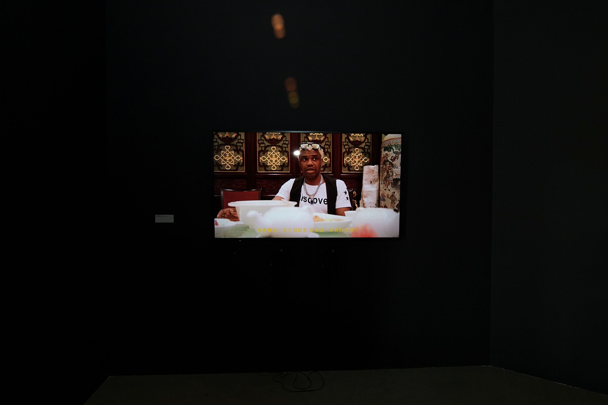 Video of a man at a table projected on a dark wall.