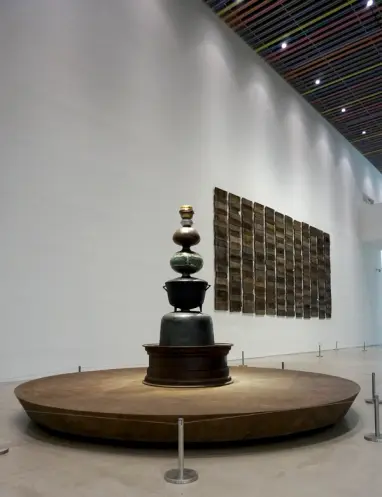 A spacious gallery displays a large mixed-media sculpture in the center of the room, with accompanying wall art in the sur...