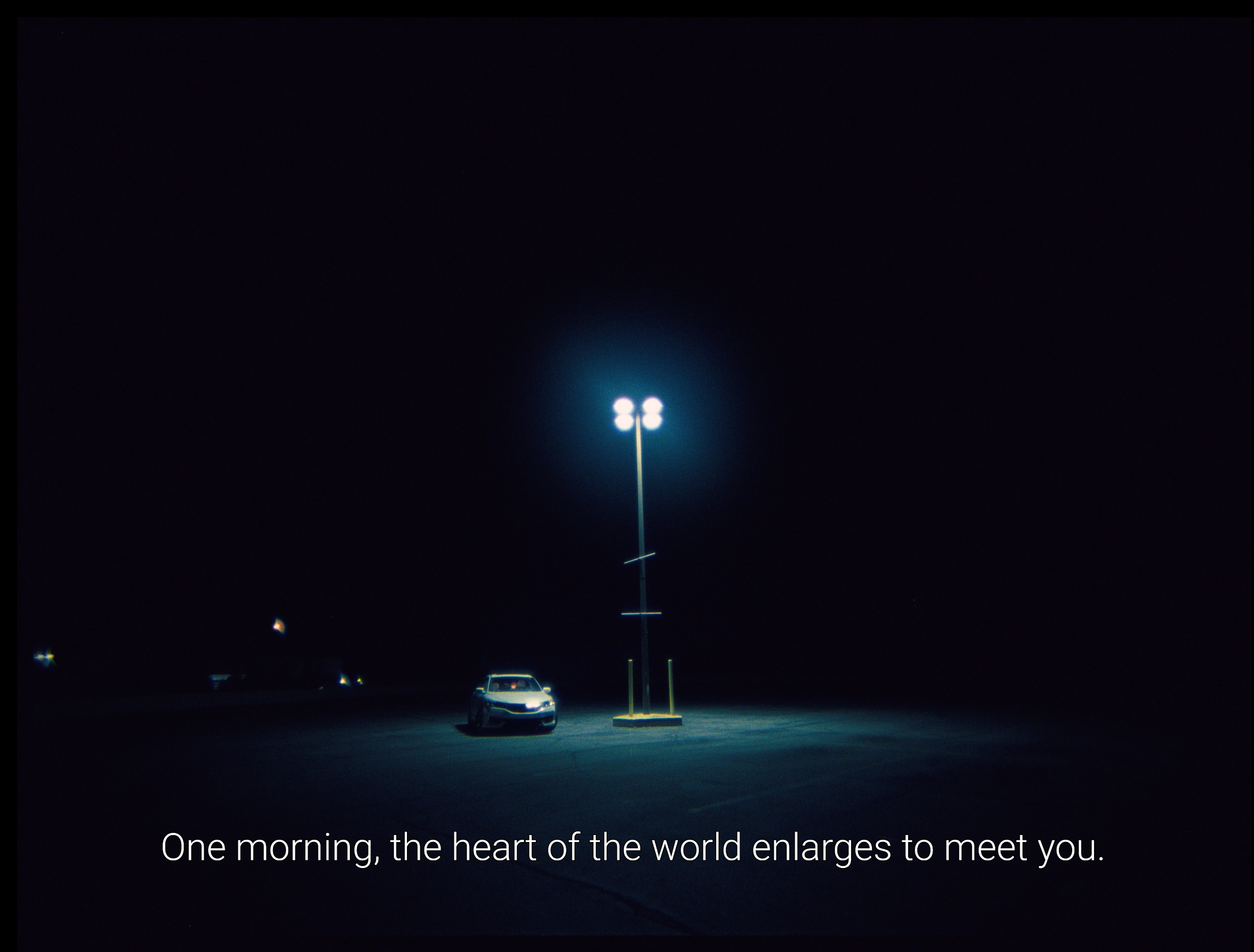 A car parked under a lone streetlight at night with the caption, "One morning, the heart of the world enlarges to meet you."