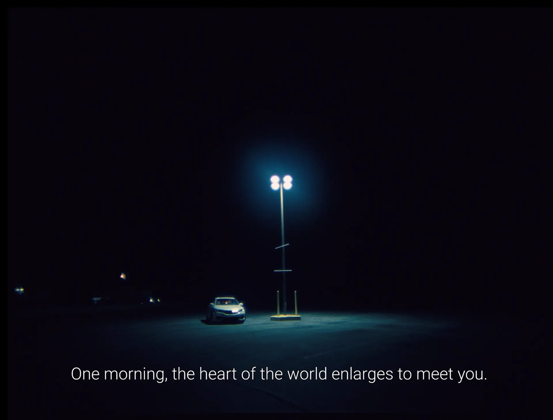 A car parked under a lone streetlight at night with the caption, "One morning, the heart of the world enlarges to meet you."