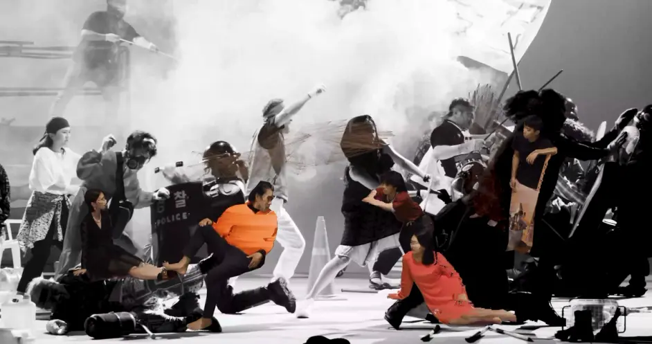 A dynamic scene depicting distorted human forms in costumes and riot gear engaging in apparent conflict, set in a foggy at...