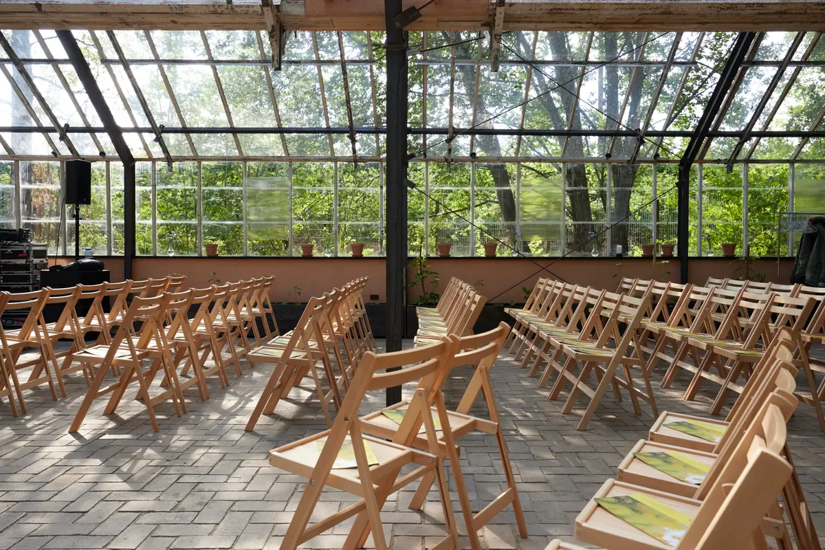 Several folding wooden chairs neatly arranged in rows inside a spacious, naturally lit greenhouse space.