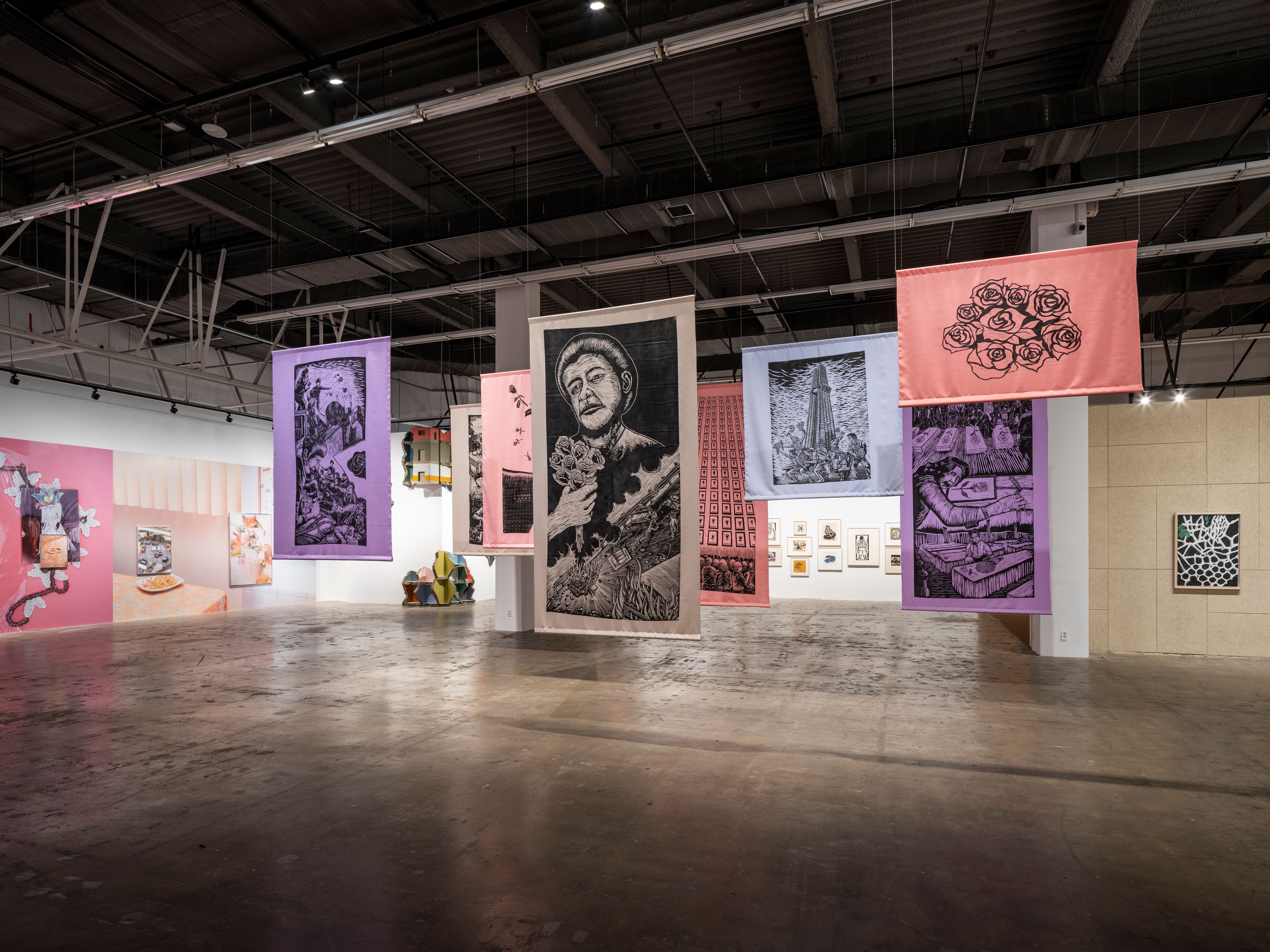 A collection of woodcut screen prints suspended from a gallery ceiling.