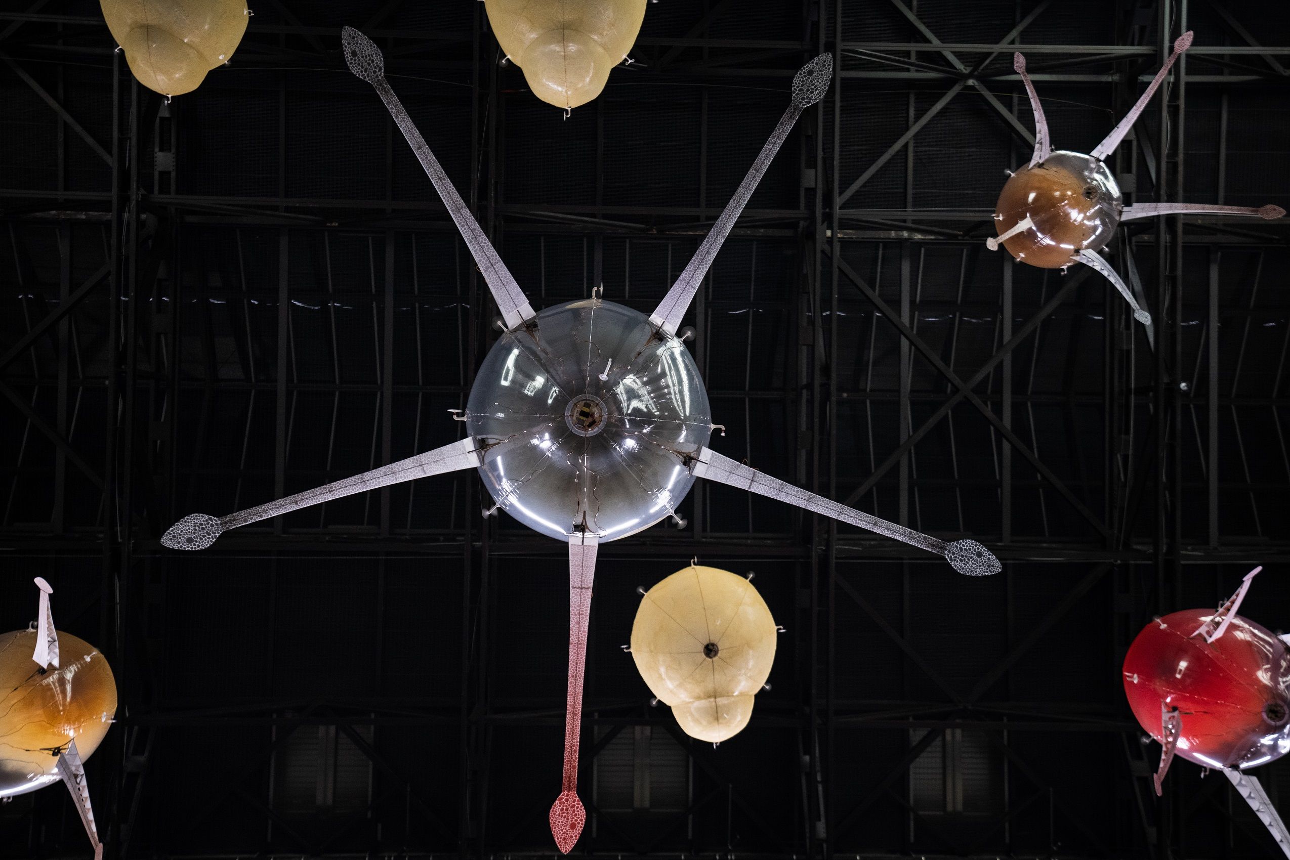 An installation in an industrial-styled gallery hall featuring a ceiling lamp shaped like an octopus with snake-headed ten...