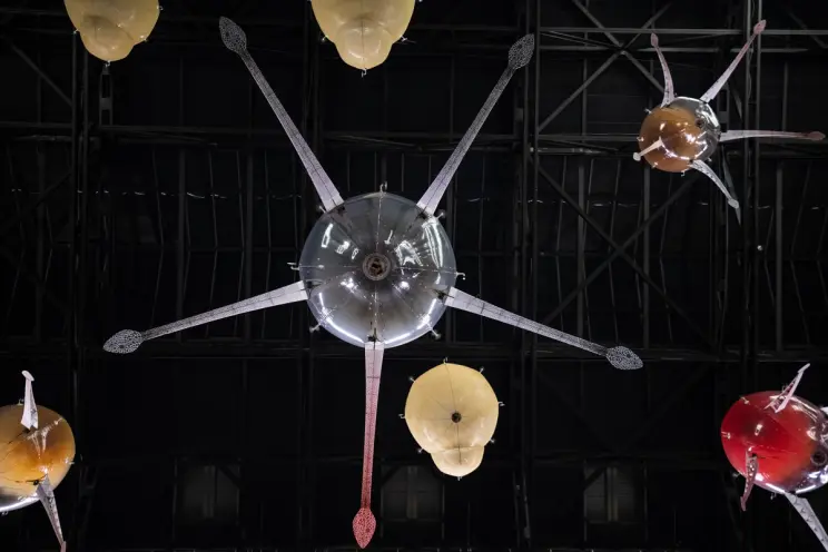 An installation in an industrial-styled gallery hall featuring a ceiling lamp shaped like an octopus with snake-headed ten...