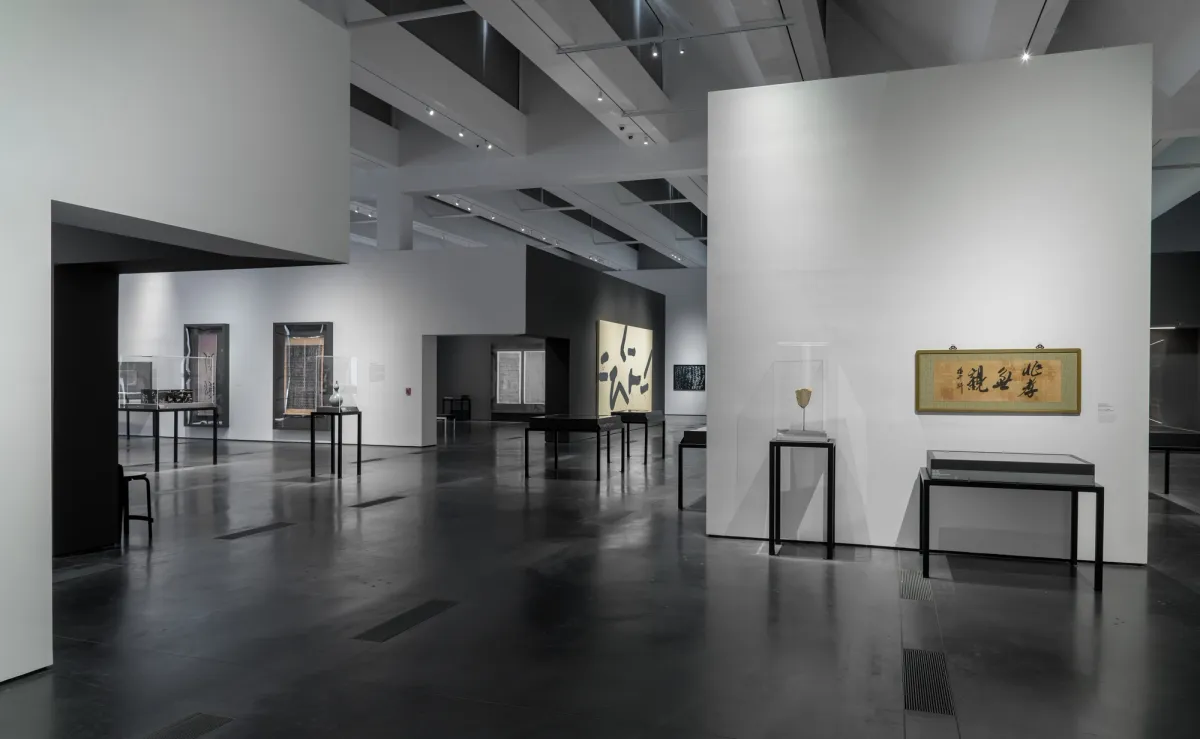 A gallery room with dark flooring and white walls, displaying a variety of art pieces related to the Art of Korean Writing exhibition at the Los Angeles County Museum of Art.