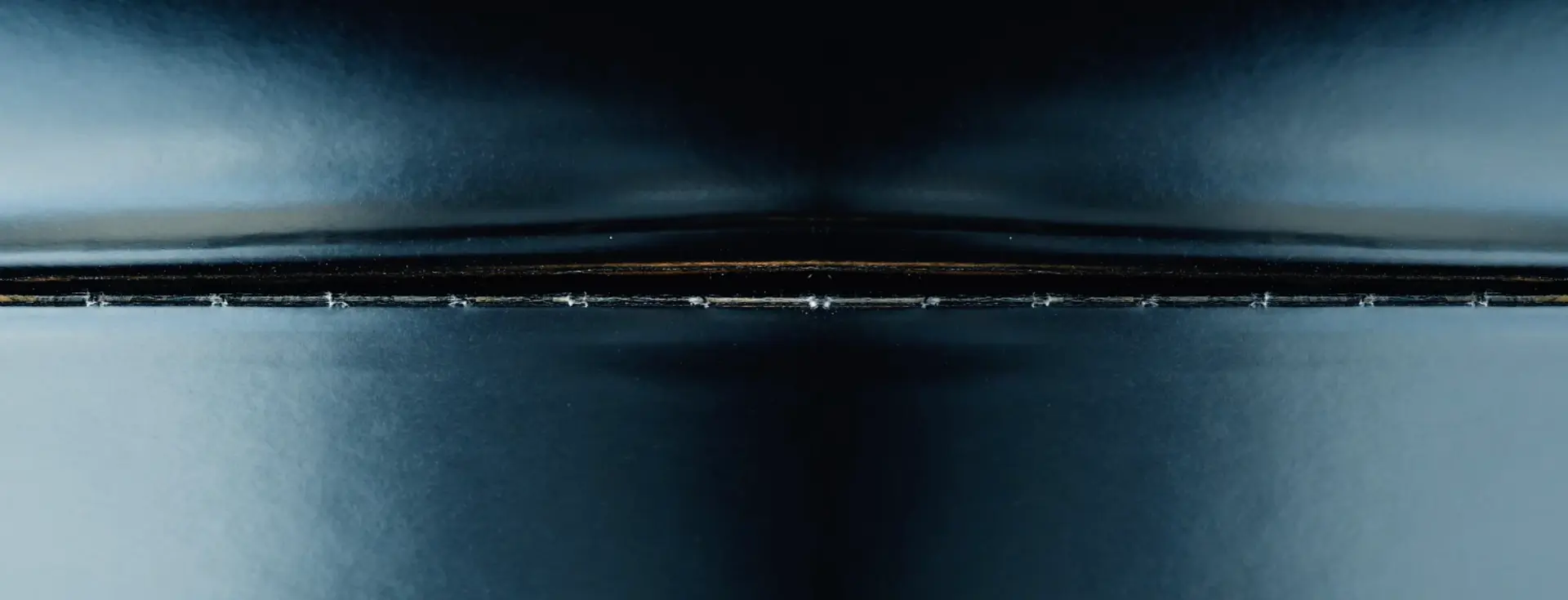 A large blue and grey horizontal shape, reminiscent of a horizon line, emerges from a pitch-black background.