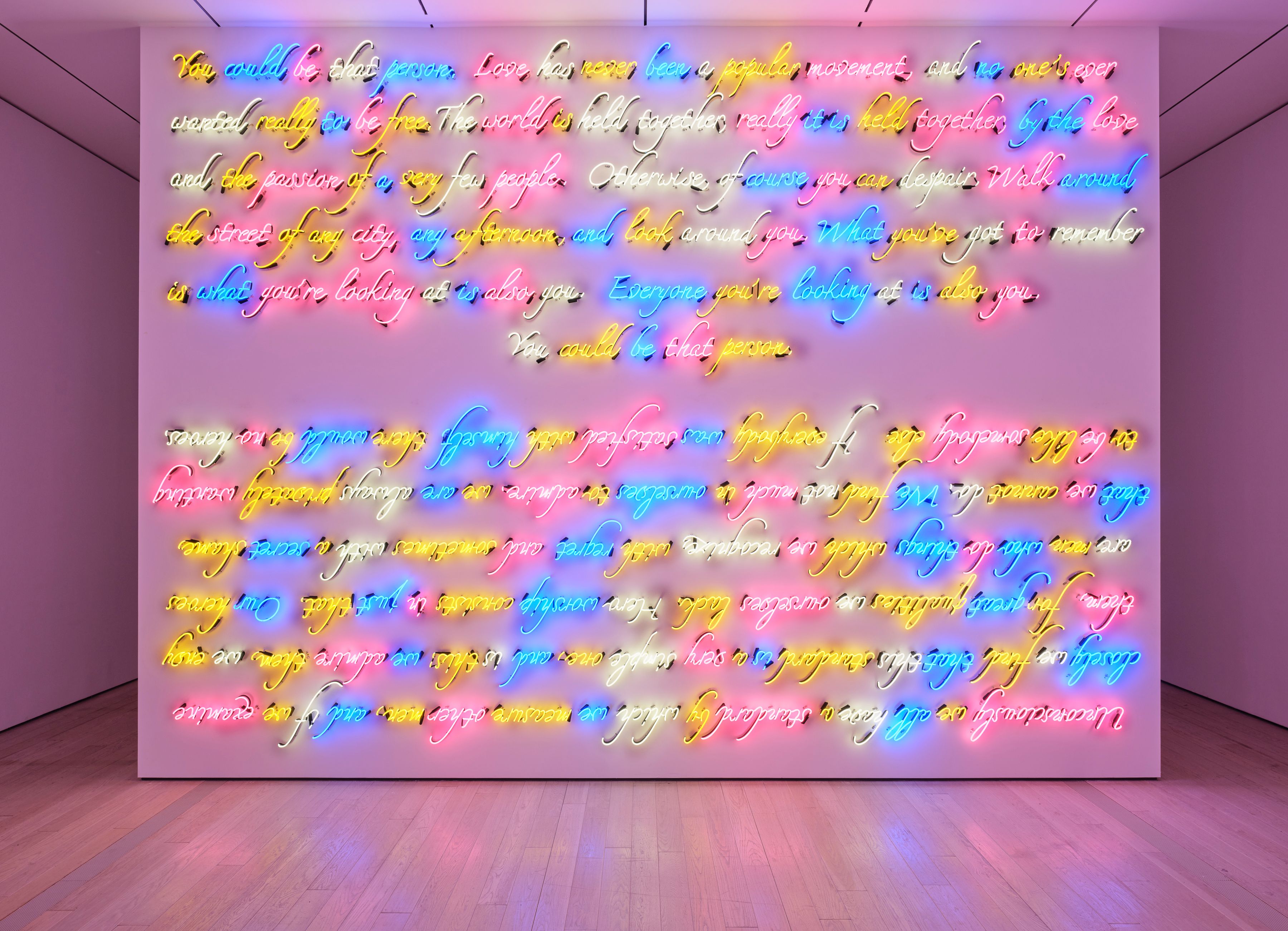 Full frontal view of expansive neon cursive text artwork filling a wall, radiating colorful light across the floor.