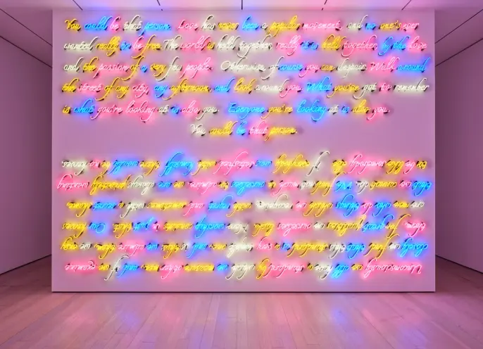 Full frontal view of expansive neon cursive text artwork filling a wall, radiating colorful light across the floor.