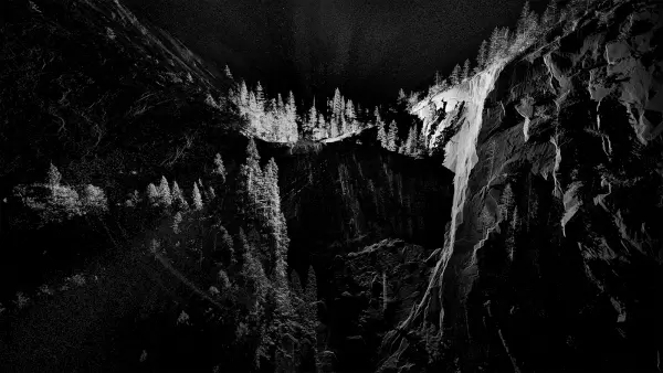 A striking black and white image showcases a cave in deep perspective. The high contrast highlights the sharp textures and contours of the cave's inner surface.