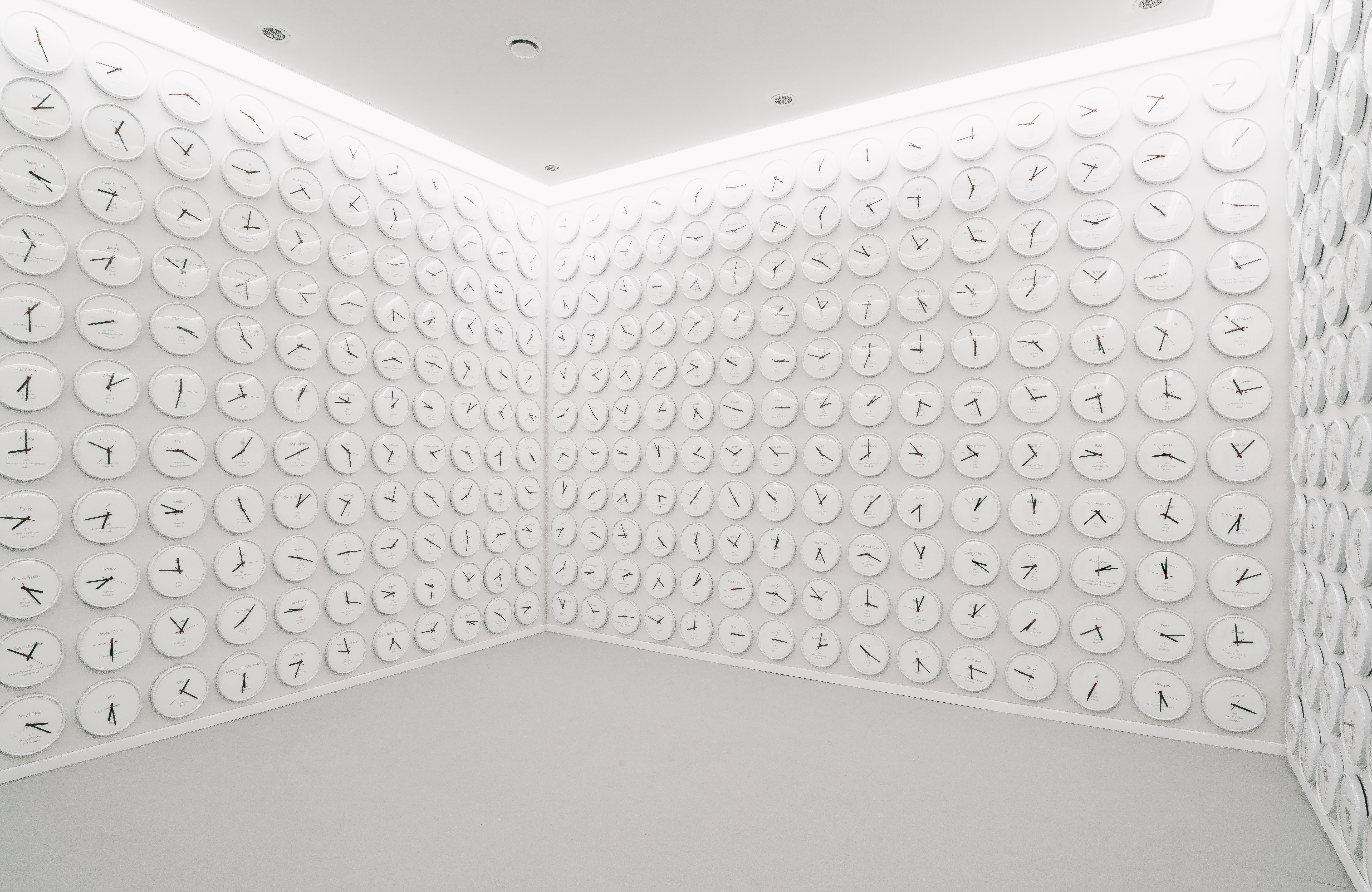 A wide room with walls entirely covered in round white clocks displaying various time zones.