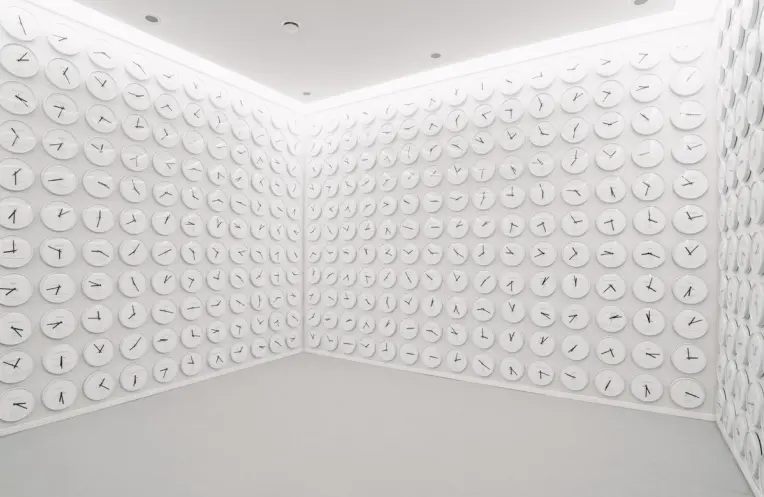 A wide room with walls entirely covered in round white clocks displaying various time zones.