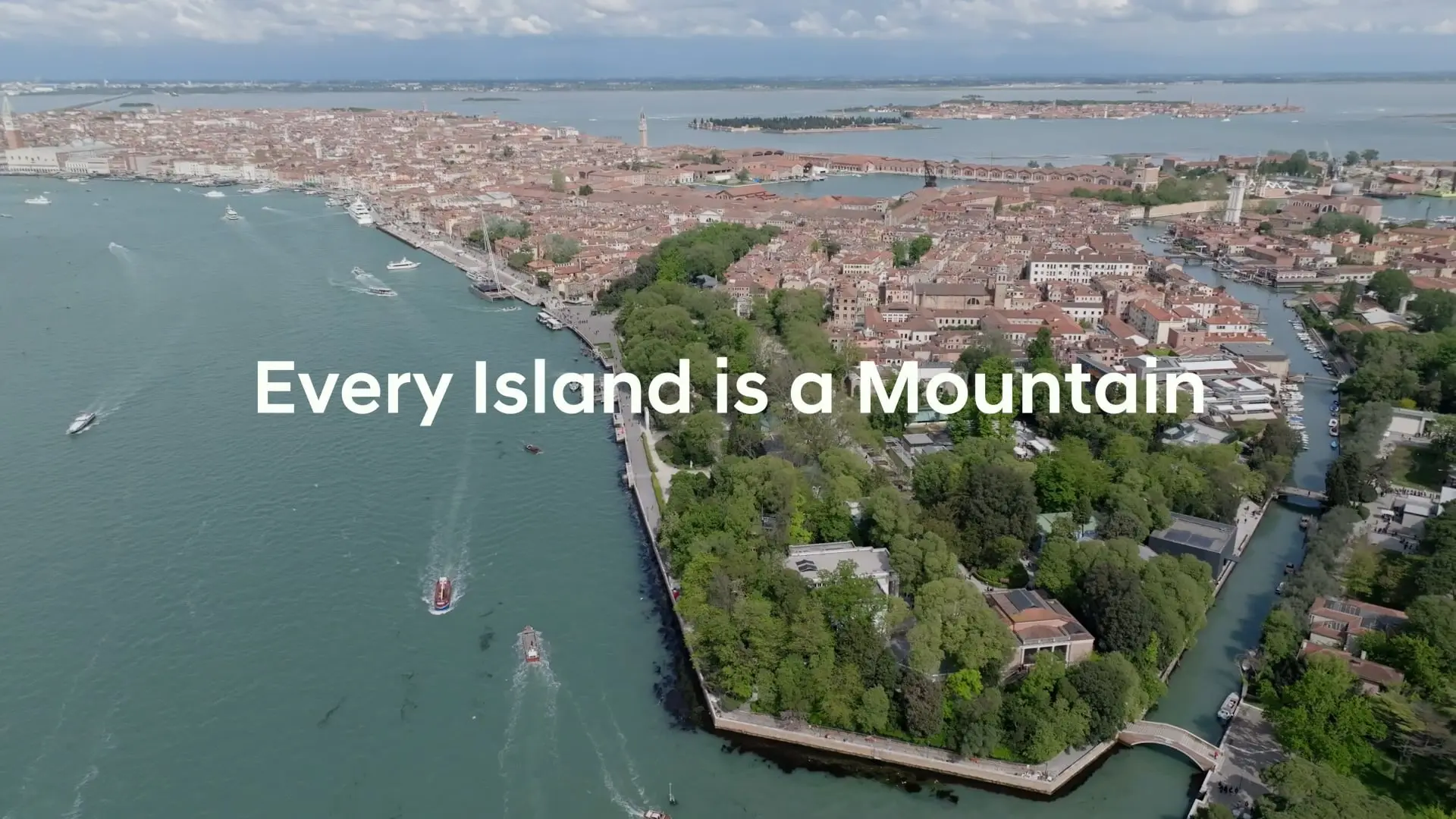 Aerial view of a historic city surrounded by waterways and greenery, with text overlay: "Every Island is a Mountain."