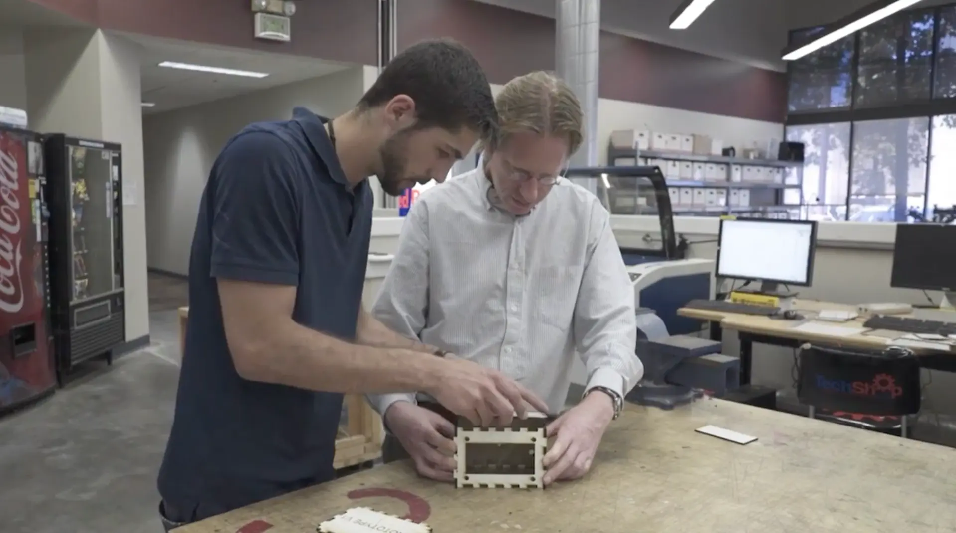 Two individuals assembling components on a table in a sophisticated workshop environment.