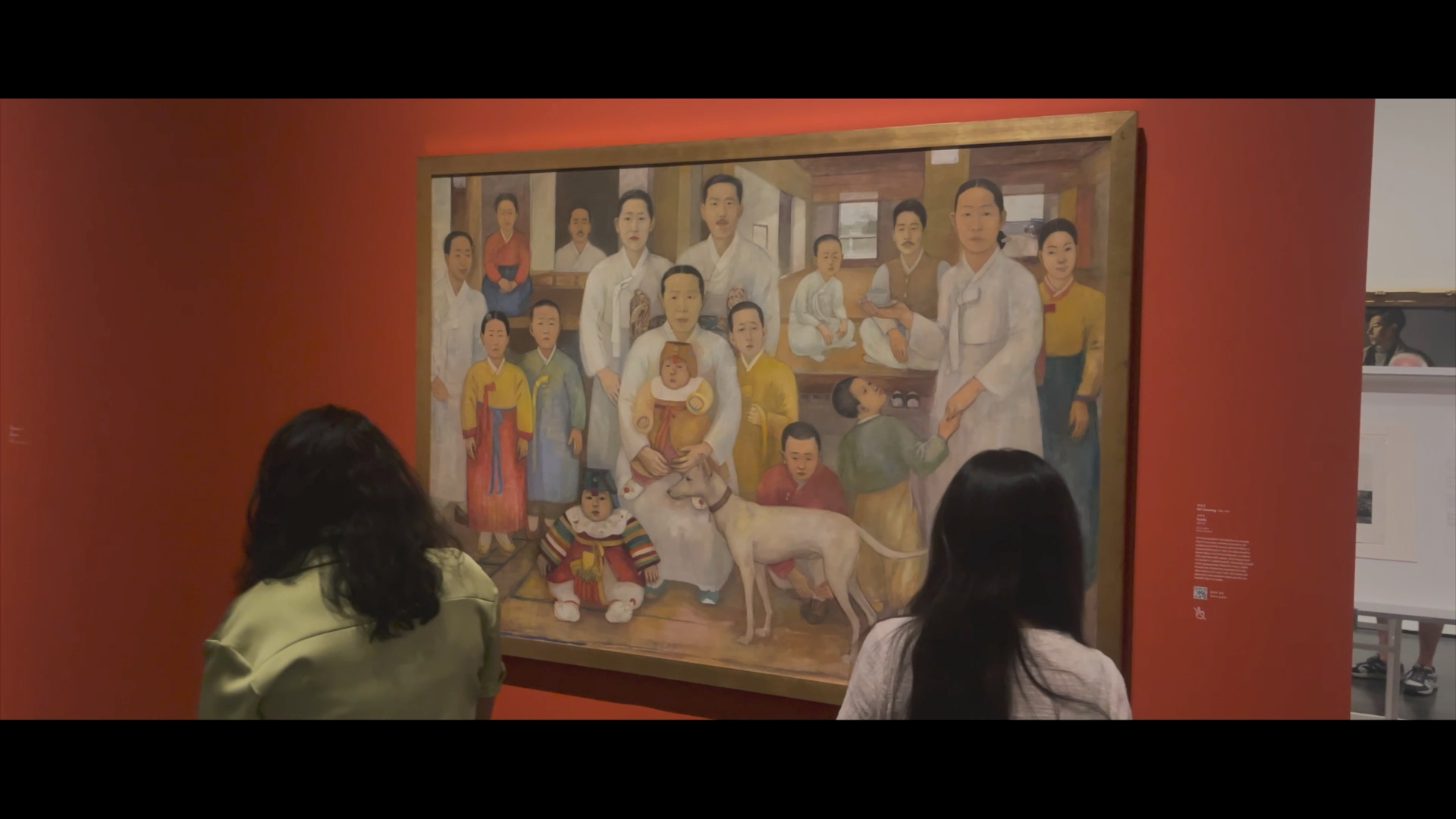 Two individuals observing a framed family portrait hanging on a vibrant red wall.
