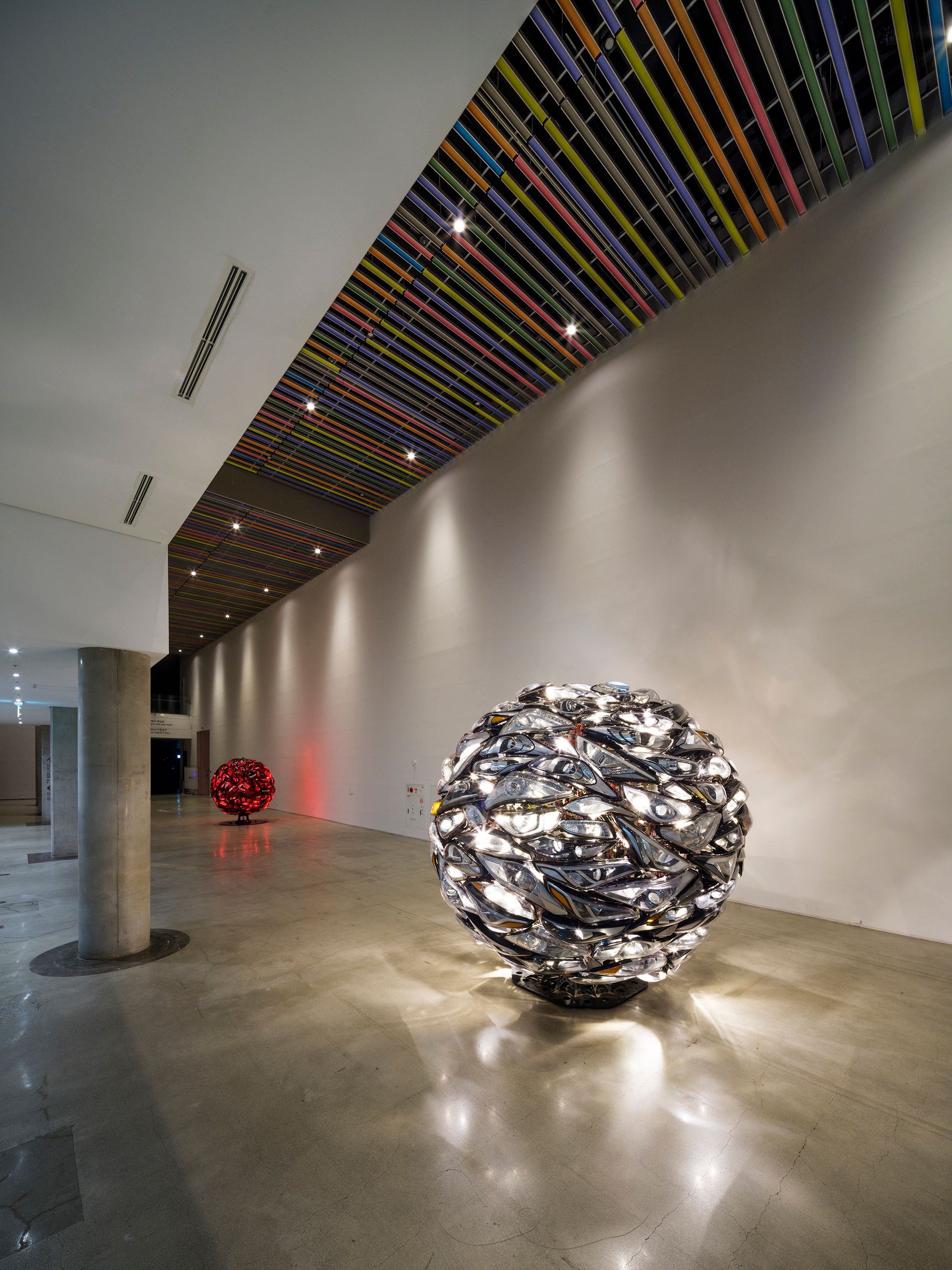 Two large, spherical metallic sculptures, one made of shiny red and silver materials and the other made of steel, dominate...