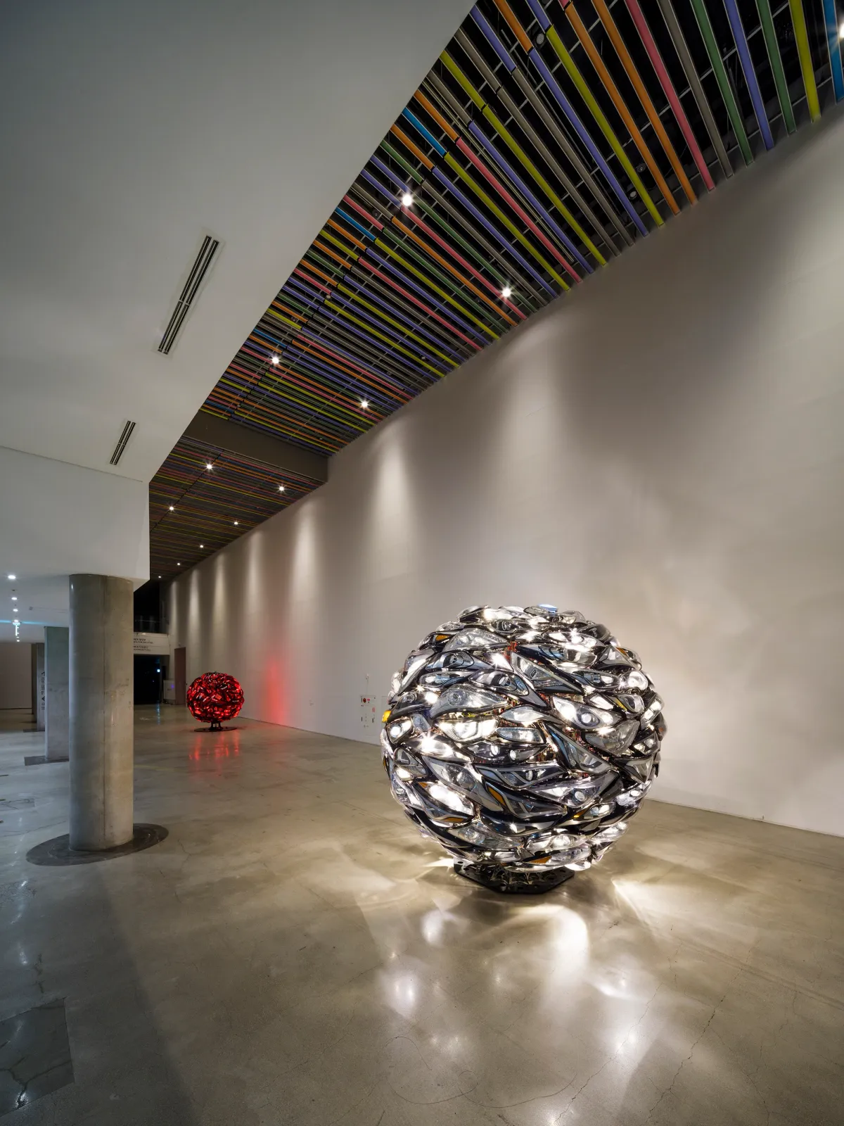 Two large, spherical metallic sculptures, one made of shiny red and silver materials and the other made of steel, dominate a spacious room. The sculptures reflect Hyundai Motor's headlights and tail lights.
